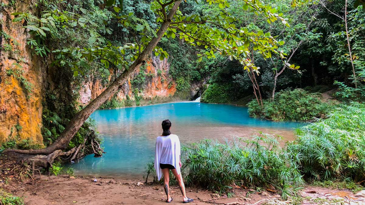 Woman stands on the bank of a bright blue pool at Bassin Bleu, Haiti