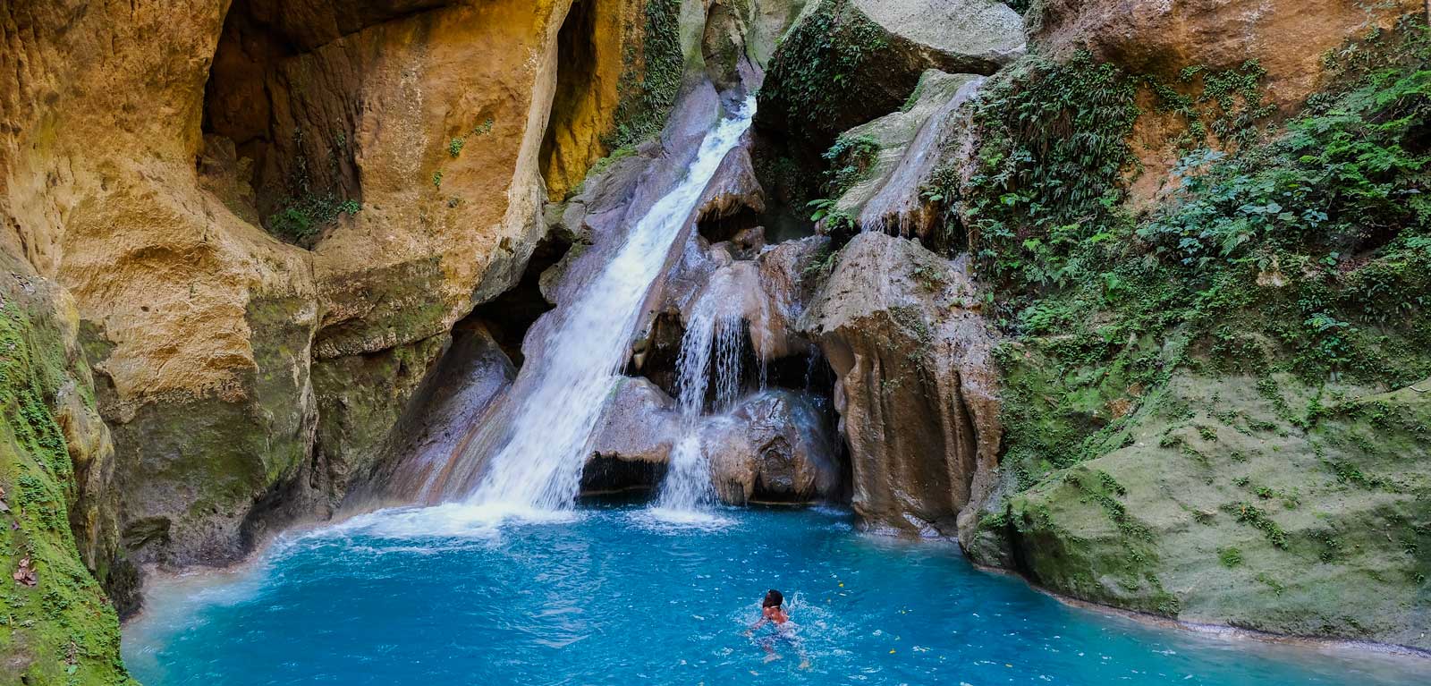 Person swimming beneath a waterfall in Bassin Bleu, Haiti