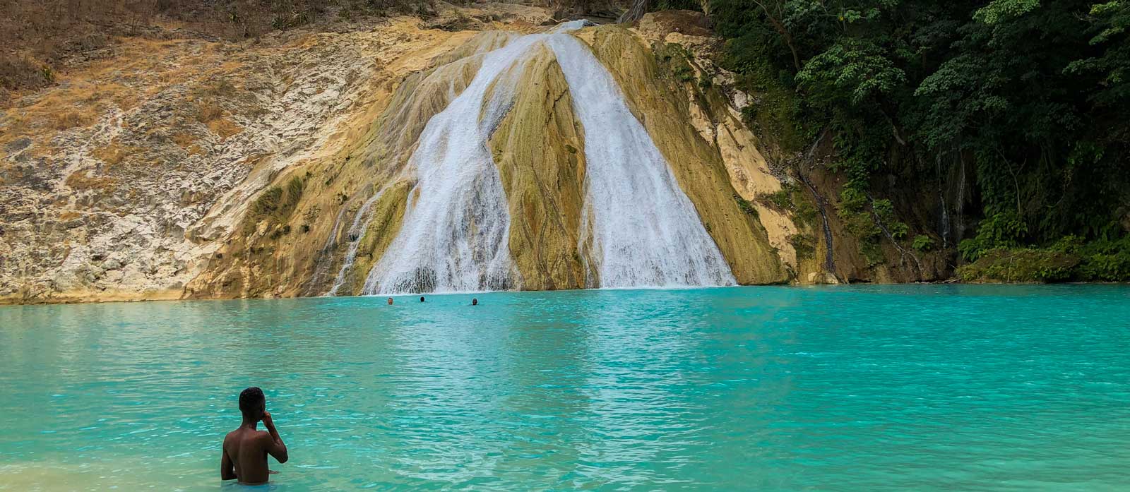 People swimming beneath a waterfall in Bassin Zim, Haiti