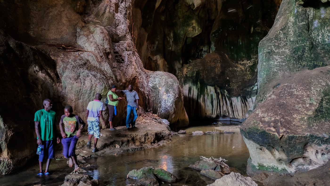 Five people walking across rocks inside the grotto of Bassin Zim, Haiti