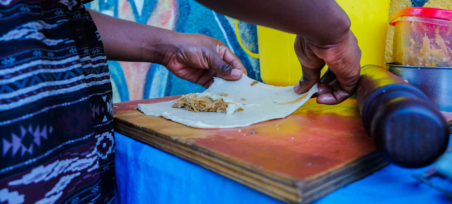 A woman making Paté Kòde at a street food stall in Haiti