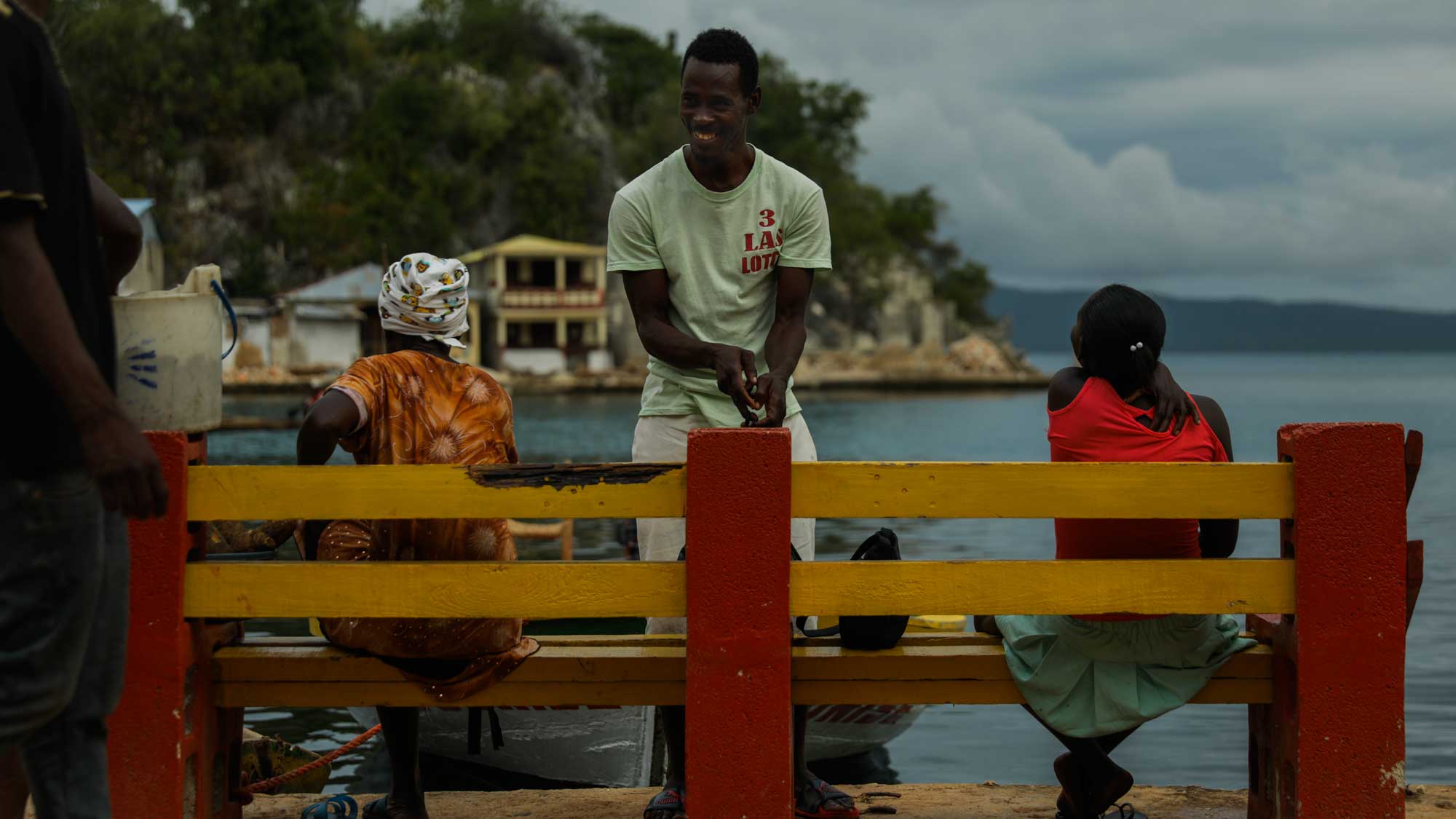 People relaxing on a waterside bench in Pestel, Haiti