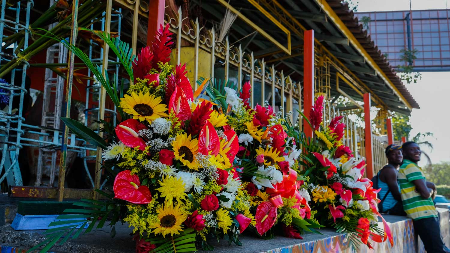 Two men smile next to flowers on display at the flower market at Place St. Pierre, Pétion-Ville