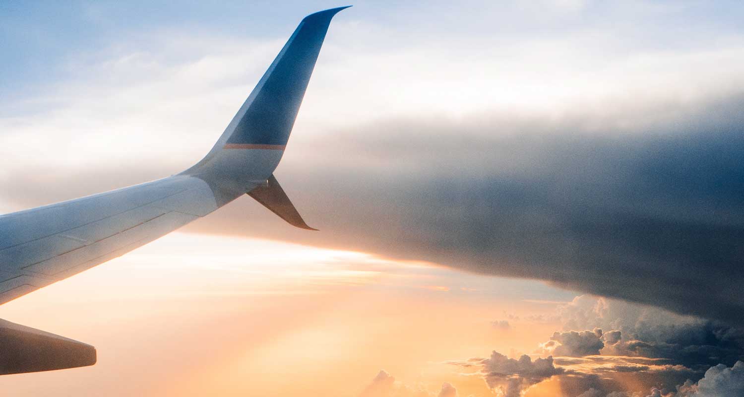 An airplane wing cuts through the clouds at sunset