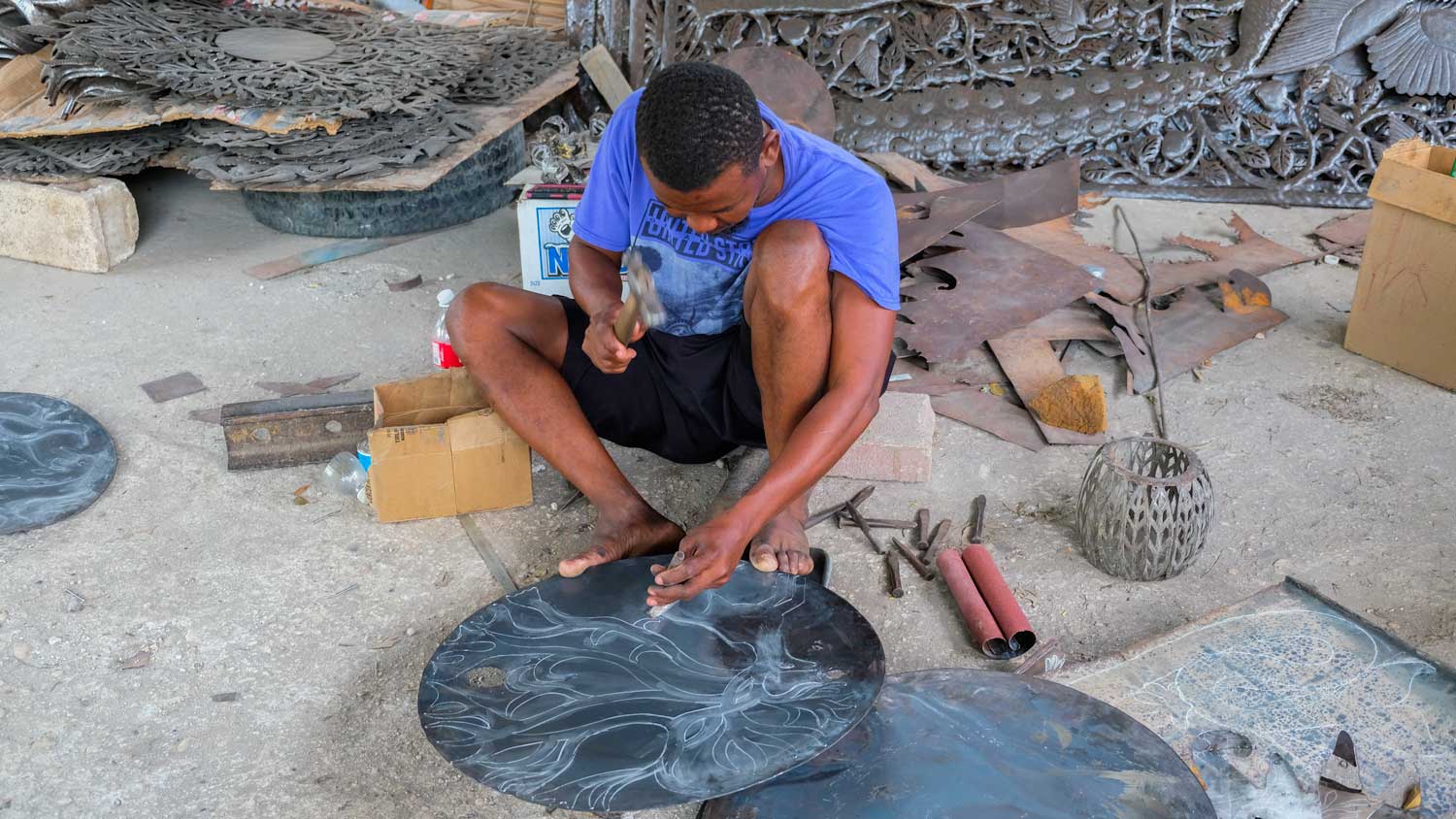 Blacksmith hammers design into metal artwork in Village Noailles, Haiti