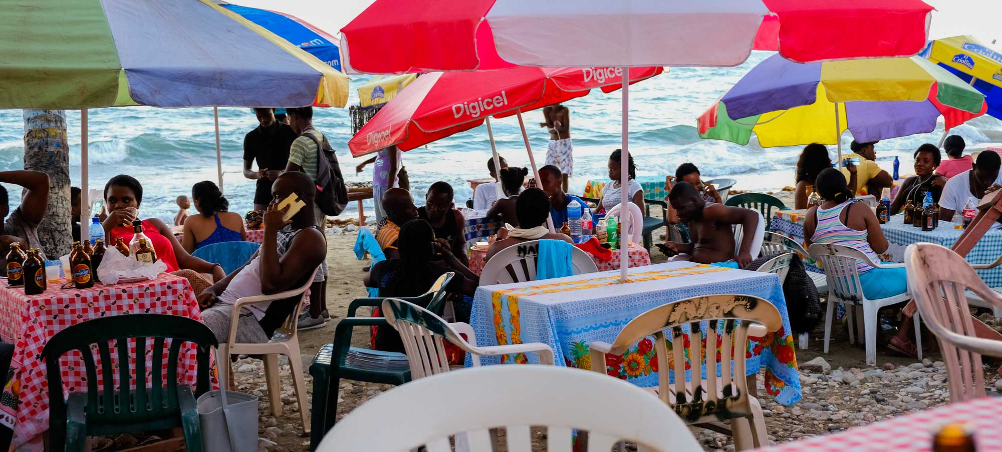 haitians relaxing and dining at table with parasols by beach