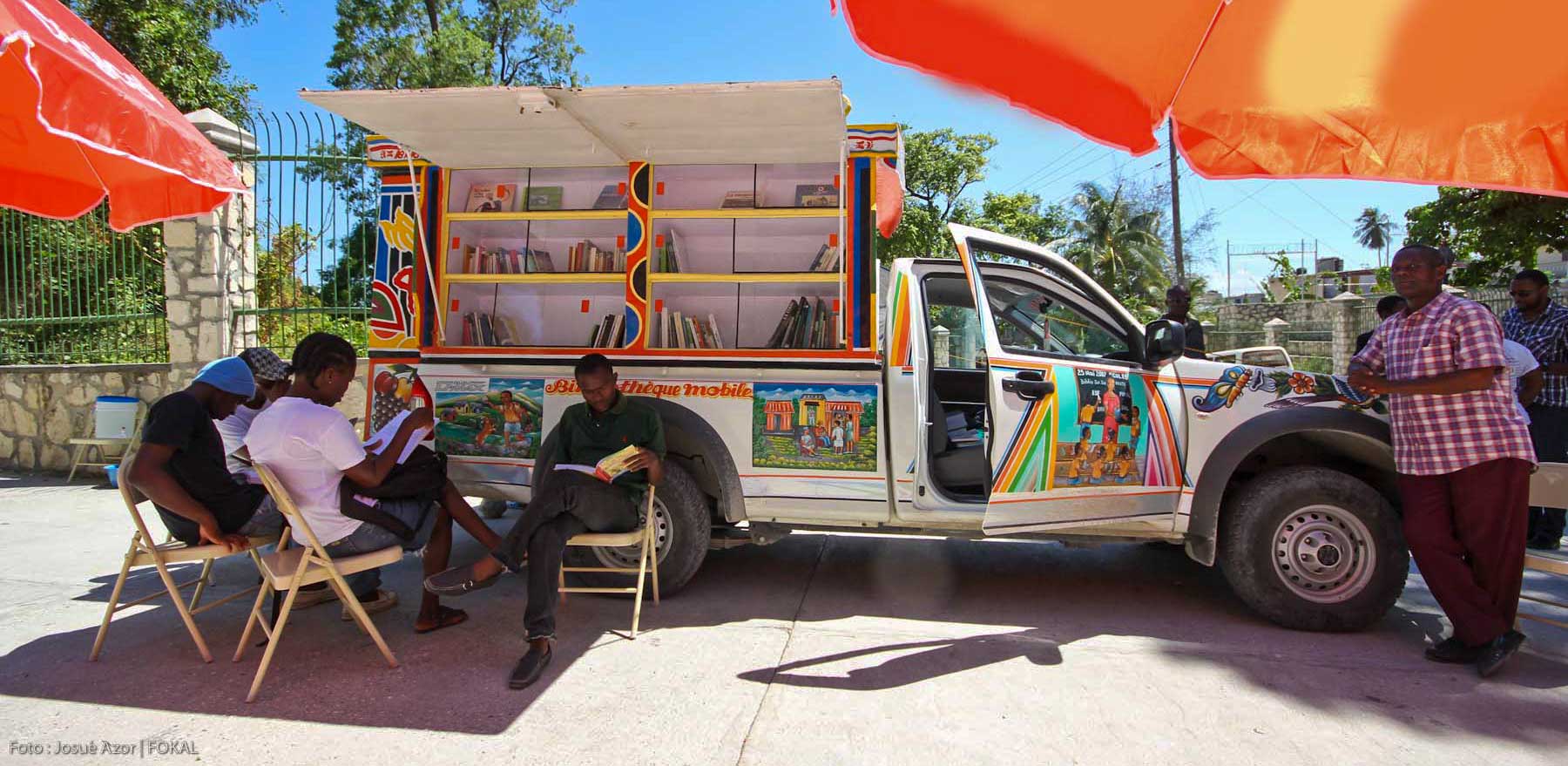 people sitting on chairs reading next to a library bus