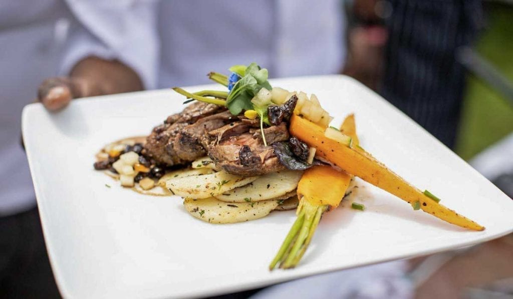 waiter holder a plate of grilled goat meat with carrots and potatoes