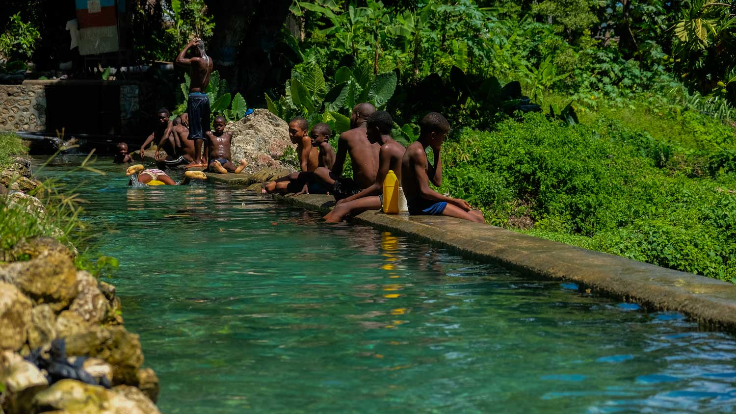 People swimming and sitting on the side of the water pools at Kay Piat, Montrouis, Haiti