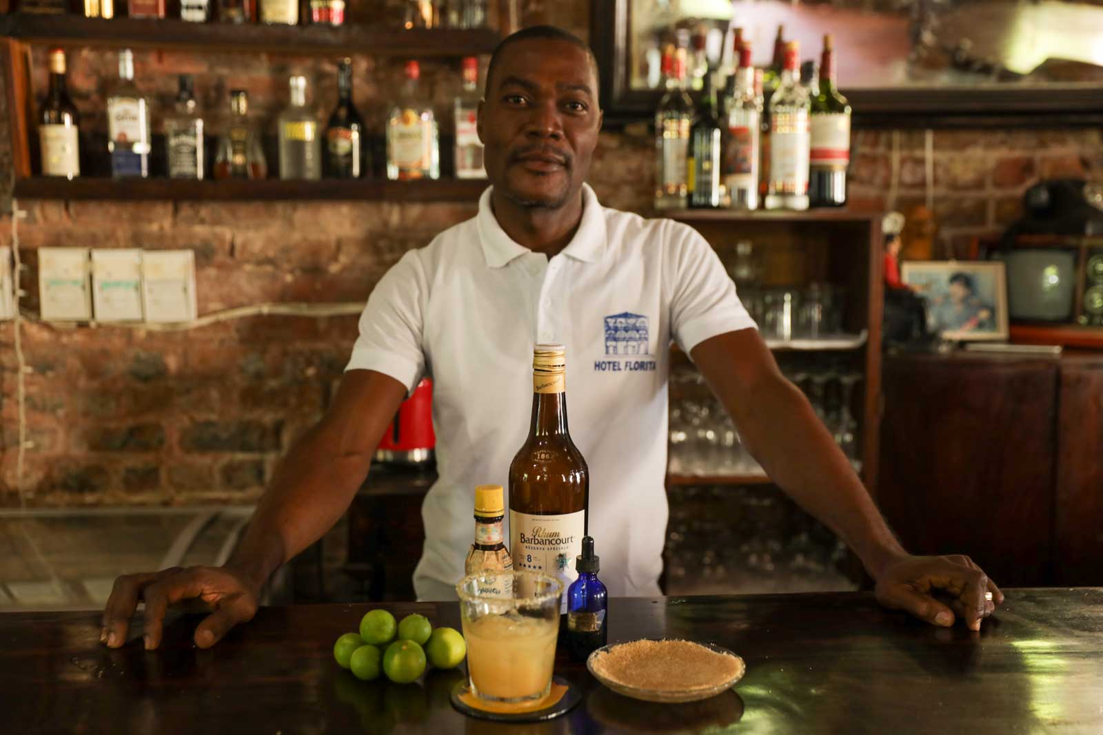 haitian bartender in bar interior presenting a rum sour