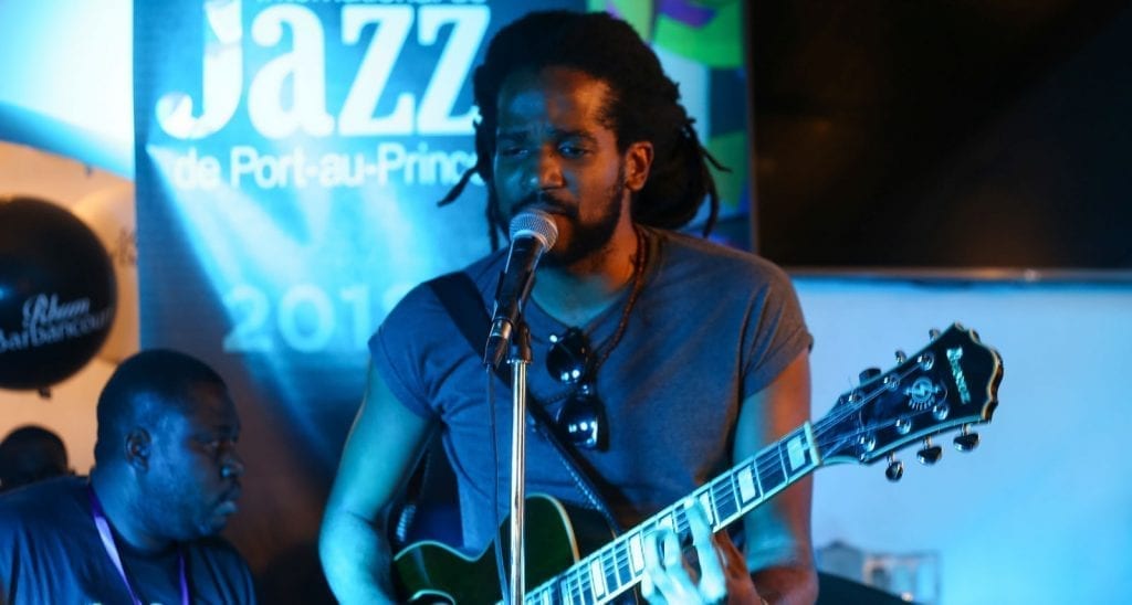 haitian musician with guitar singing on stage with microphone