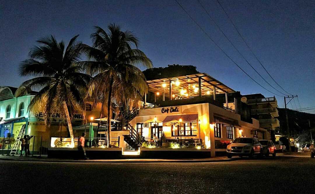 nighttime view of restaurant on a city street with palm trees