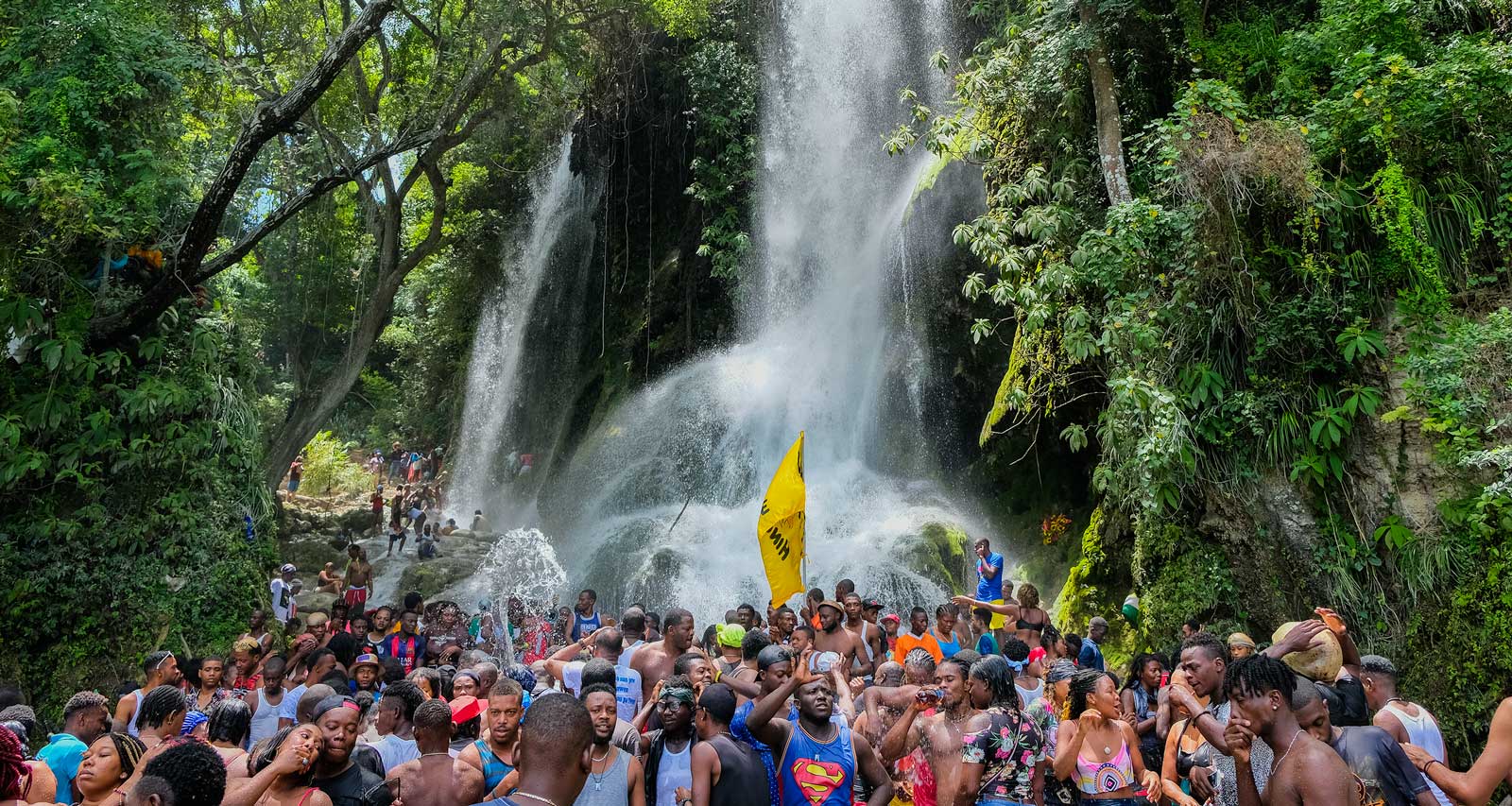 crowd of haitians standing under a huge waterfall