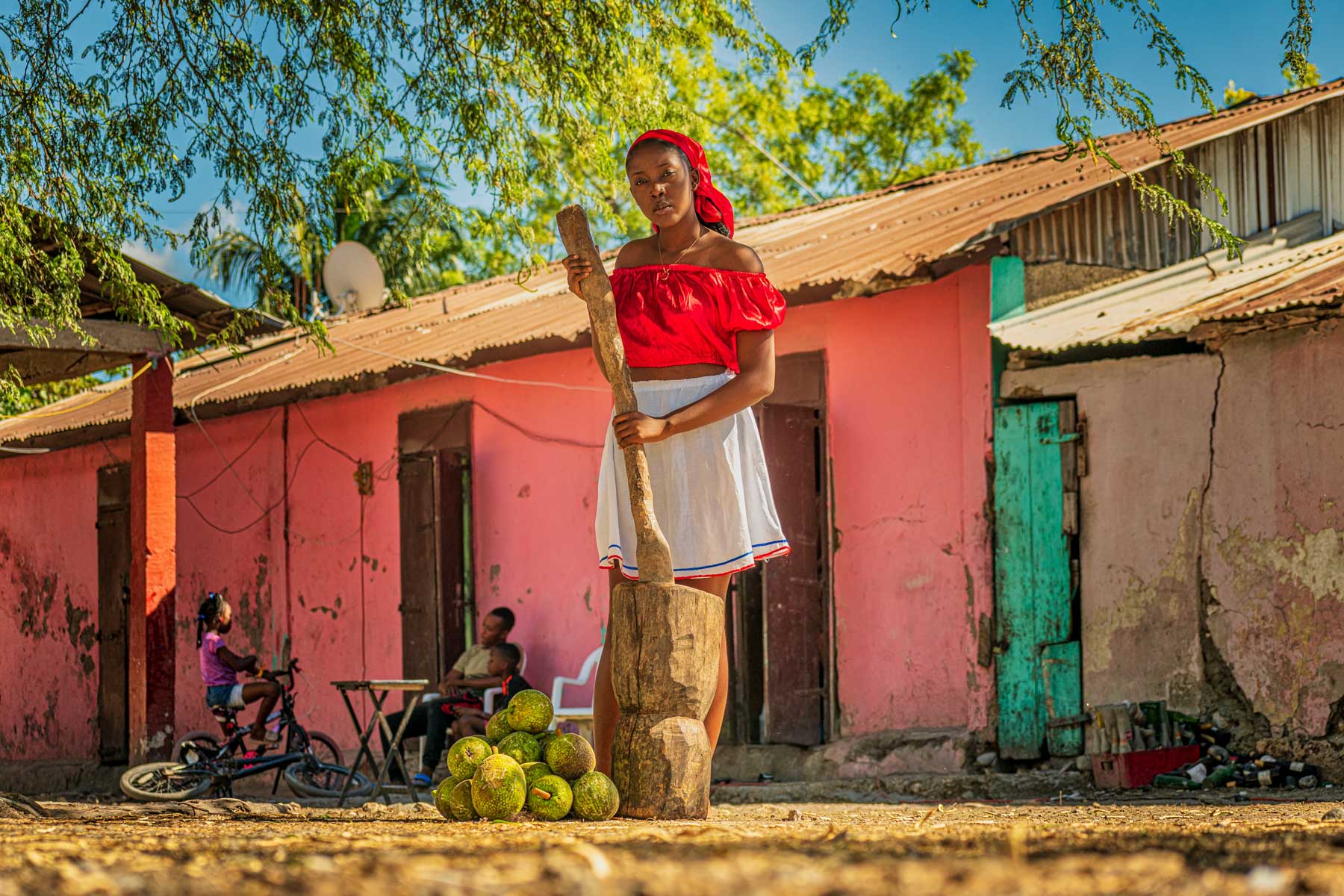 haitian girl smahing breadfruit with a big mortar in courtyard