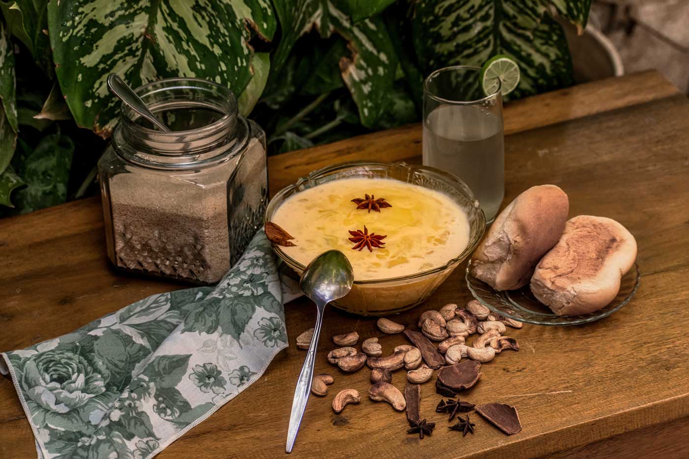 table with a bowl of haitian akasan, bread, cashew nuts, star anis and water