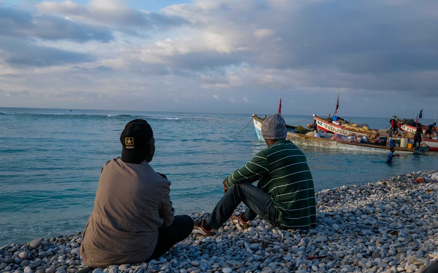 to haitian men sitting on a stony beach with boats