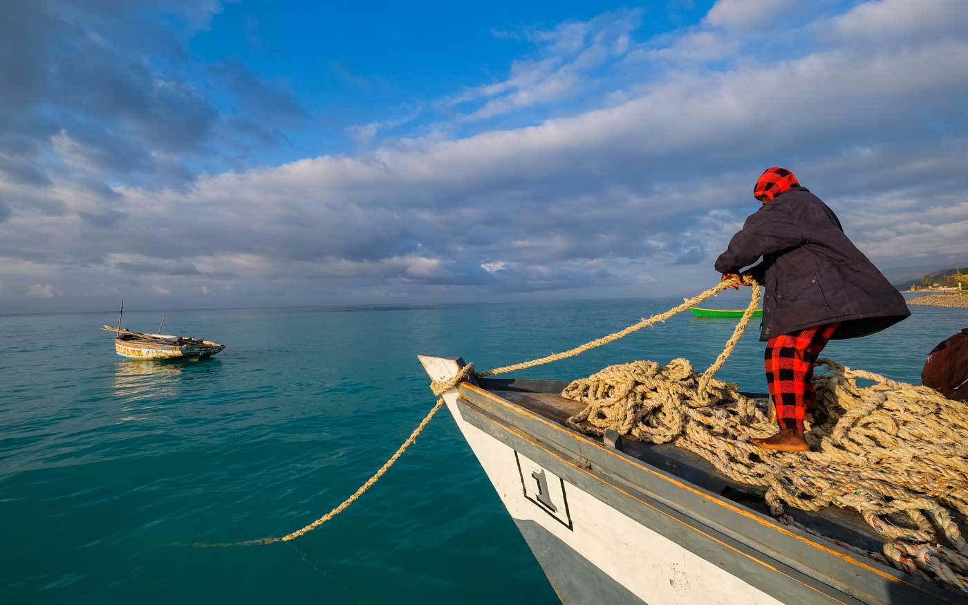 man standing on boat pulling a large rope