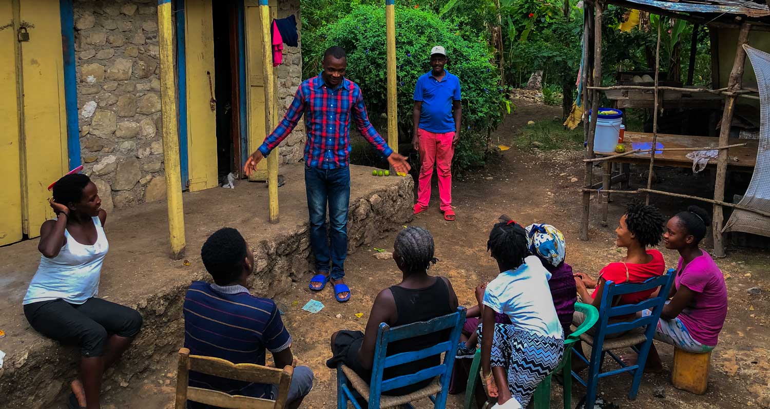 group of haitians sitting on chairs and porch in courtyard