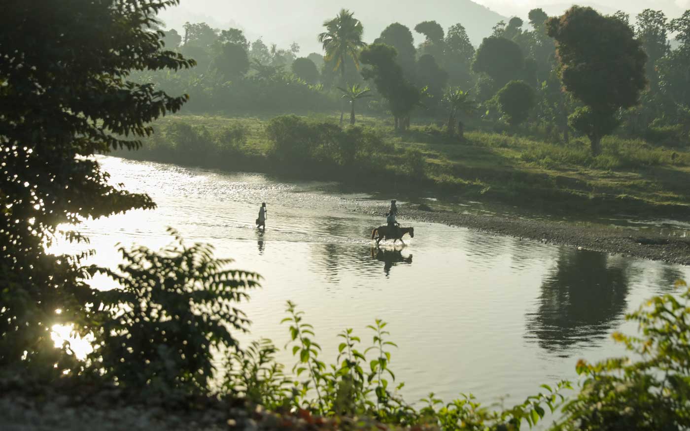 haitians crossing the grande-anse river by foot and donkey