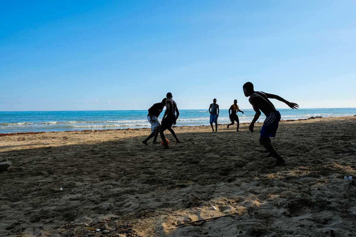 five haitian boys playing soccer on beach