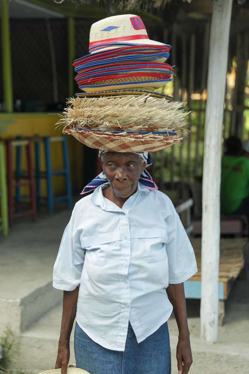 older haitian woman in white shirt wearing a stack of straw hats