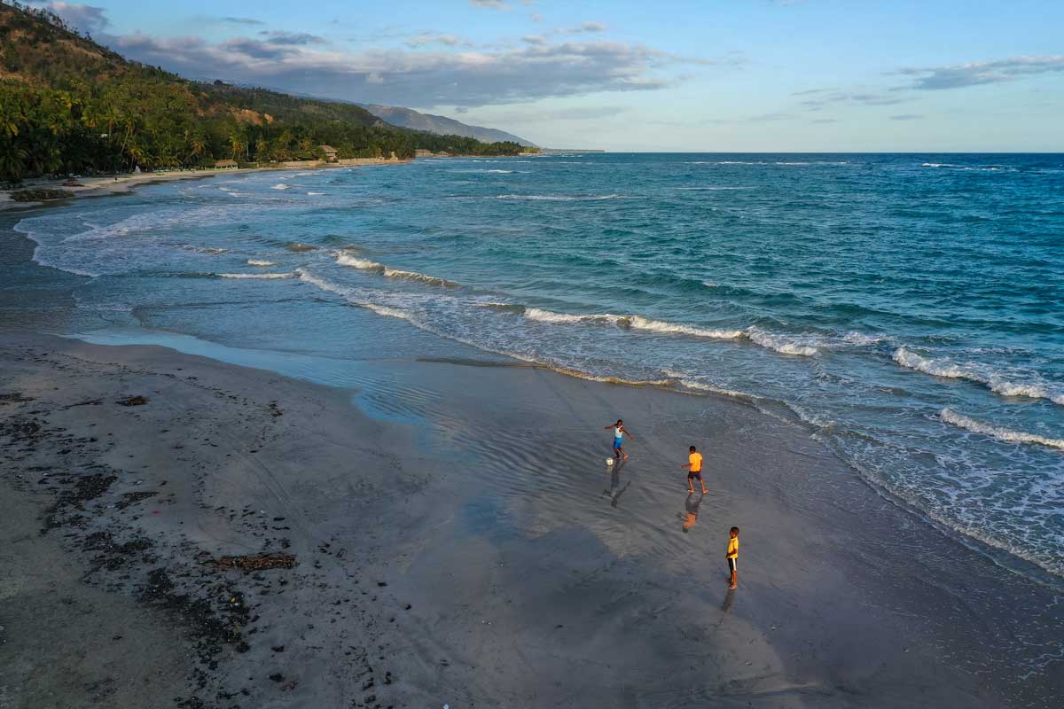 three haitian boys playing football on beach