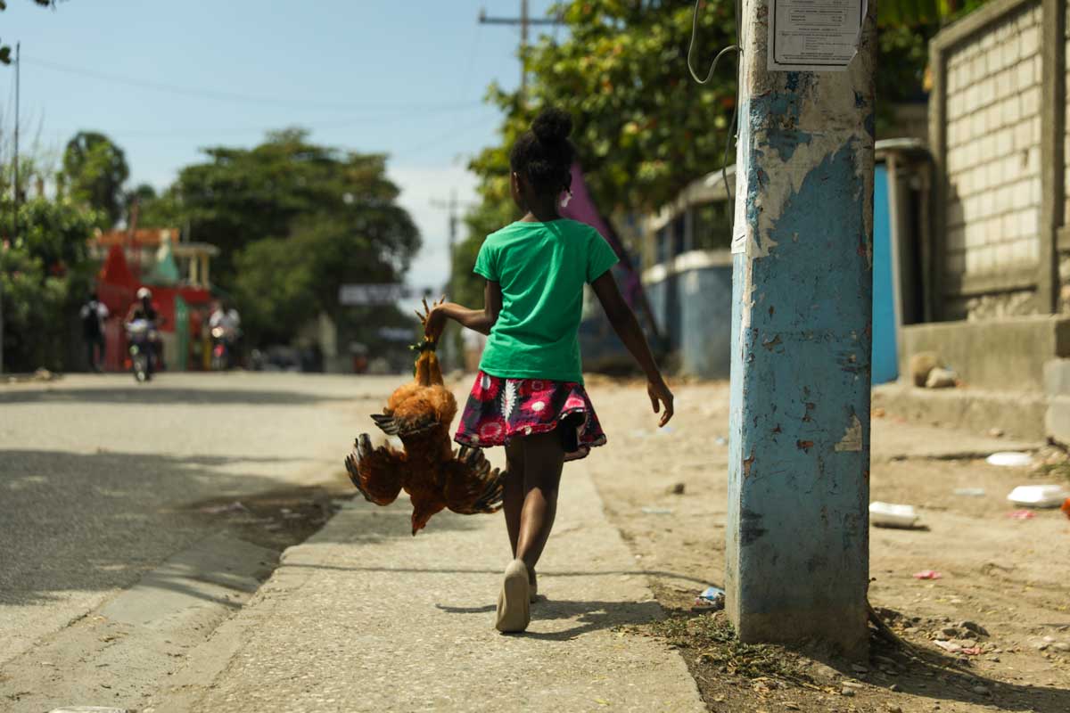 haitian girl walking on sidewalk with chicked in hand