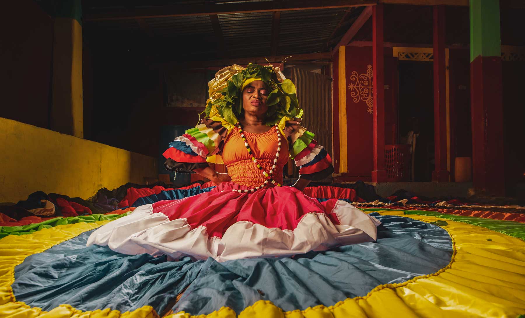 vodou priestess kneeling on floor in a huge and colorful dress