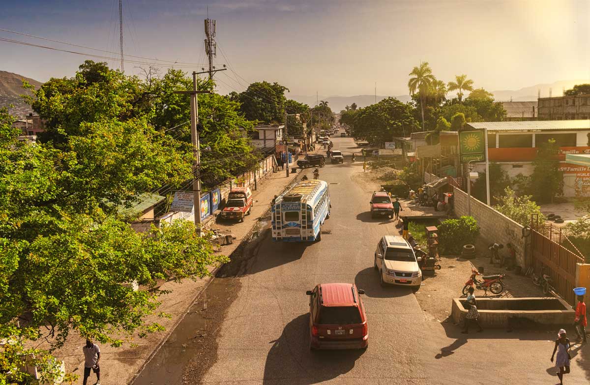 city street lined with tropical trees with traffic and a gas station