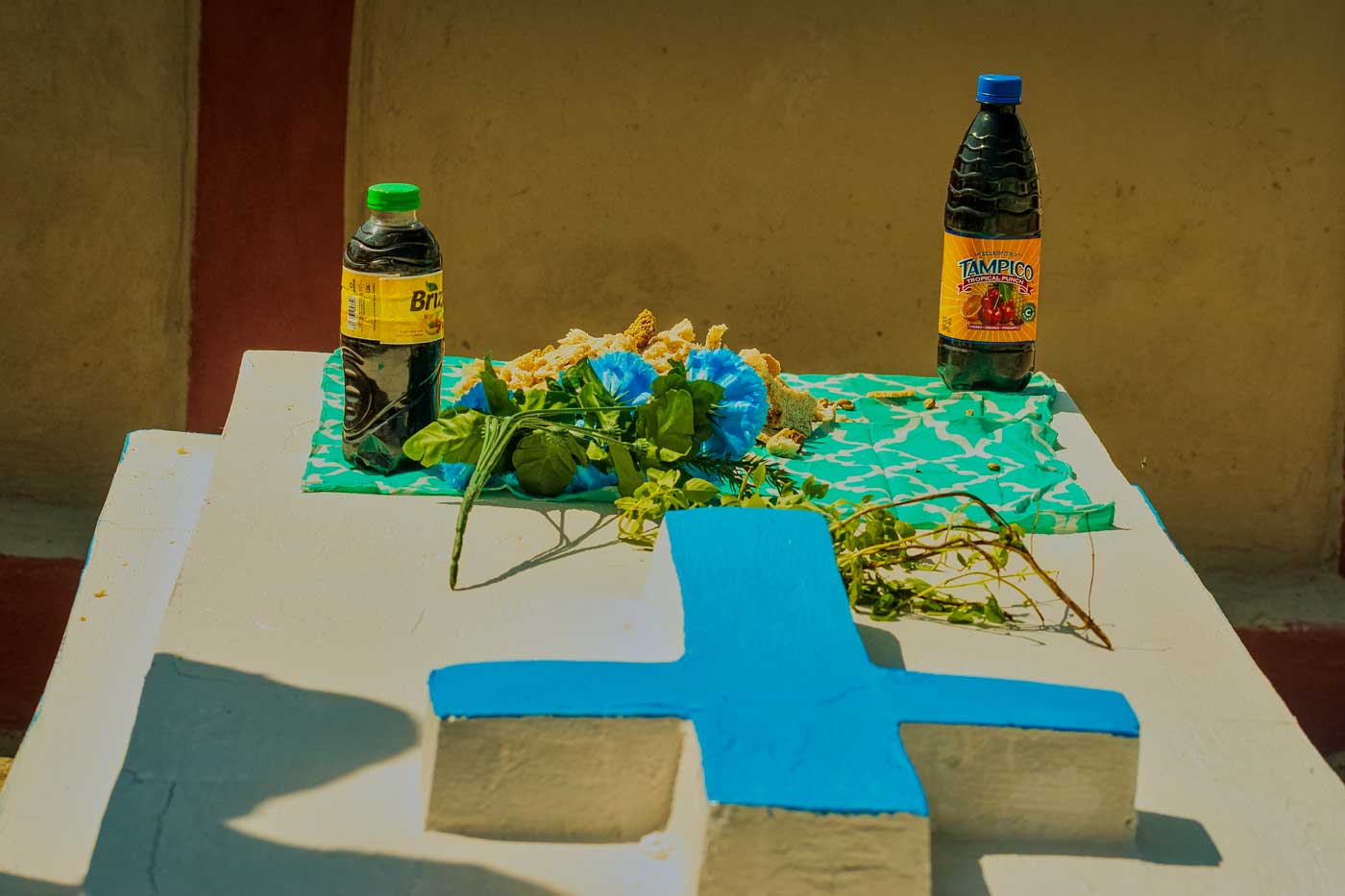 pierre tombale dans un cimetière haïtien avec deux bouteilles de soda et des fleurs